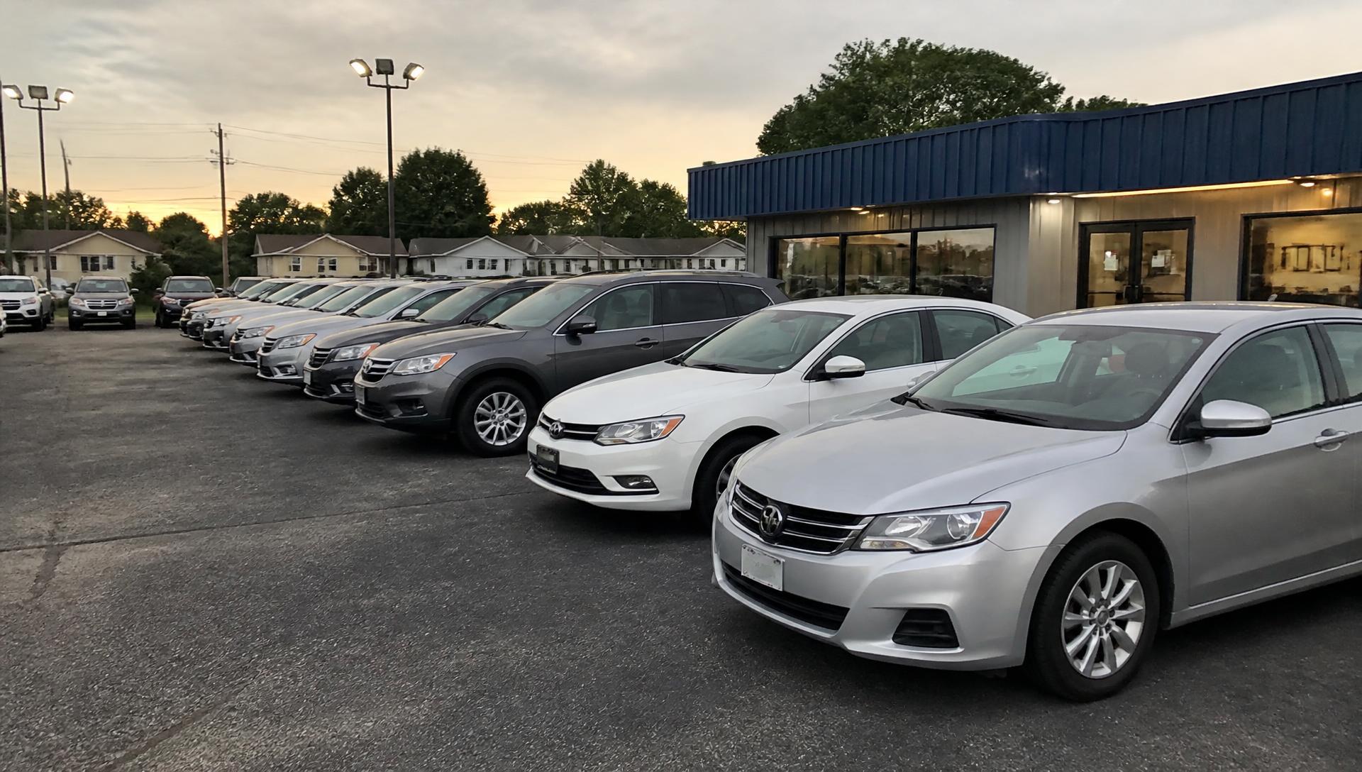 A row of pre-owned cars and SUVs parked outside a used car dealership at dusk